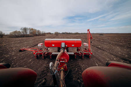 Spring sowing season. Farmer with a tractor sows corn seeds on his field. Planting corn with trailed planter. Farming seeding. The concept of agriculture and agricultural machinery.の写真素材