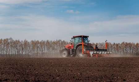 Spring sowing season. Farmer with a tractor sows corn seeds on his field. Planting corn with trailed...