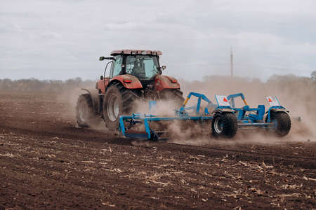 Spring sowing season. Farmer with a tractor sows corn seeds on his field. Planting corn with trailed...