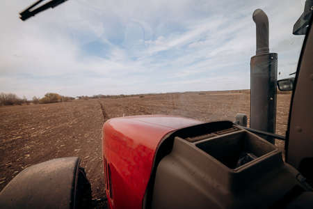 Spring sowing season. Farmer with a tractor sows corn seeds on his field. Planting corn with trailed...