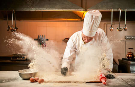 Professional pastry chef prepares dough with flour to make bread, Italian pasta or pizza. Flour is...