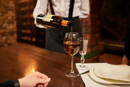The waiter in uniform pours visitors wine in restaurant