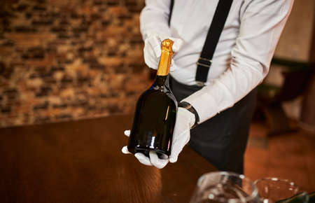 The waiter in uniform offers visitors wine in restaurantの写真素材