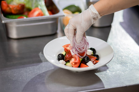 The chef in the kitchen imposes freshly chopped onions and prepares a Greek salad. Concept of Ñooking vegetarian saladの写真素材