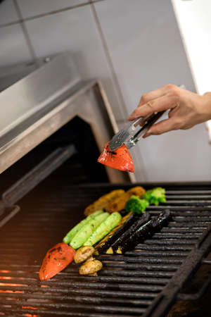Grilled vegetables: tomatoes, corn, eggplant, zucchini, mushrooms, sweet peppers are prepared in a professional grill machine. Chef grills vegetables in the restaurant kitchenの写真素材