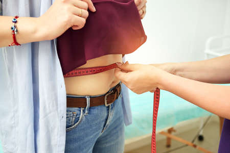 Cropped view of nutrition expert measuring waist of young woman patient in weight loss clinic. Doctor, nutritionist or dietitian discussing treatment with young woman and making individual diet planの写真素材