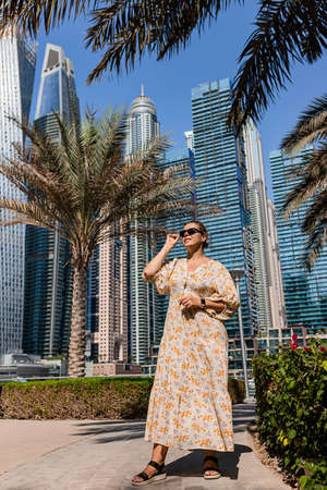 Attractive traveler woman wearing a long dress walking on a promenade in Dubai Marina district. Travel destinations and tourist lifestyle in UAEの写真素材