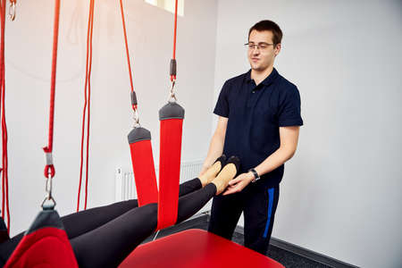 Rehabilitation specialist doing active treatment on suspension straps to female patient. Concept of...