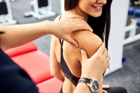 Rehabilitation specialist examining female patient before active treatment on suspension straps. Therapeutic exercises and neuromuscular activation on red cord slingsの写真素材