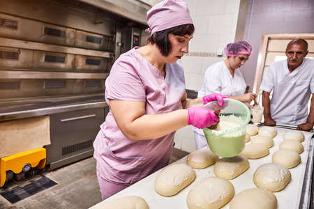 Professional baker in uniform smears butter bread dough for baking at the bakery manufacture on the...