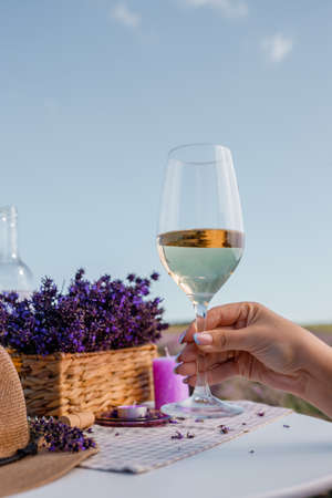 Woman hand with white wine glass on a lavander fields background in Provence, France. Lines of purple flowers bushesの写真素材