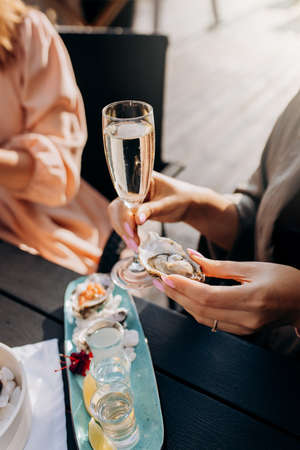 Two Women friends eating fresh oysters and drinking chilled prosecco wine on the summer sunset in restaurant. Seafood delicaciesの写真素材