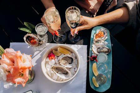 Two Women friends eating fresh oysters and drinking chilled prosecco wine on the summer sunset in...