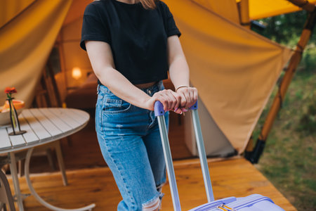 Happy woman traveler with luggage standing on background of cozy glamping house. Luxury camping tent for outdoor summer holiday and vacation. Lifestyle conceptの写真素材