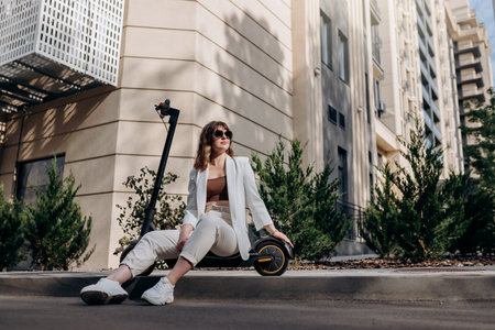 Young businesswoman in white suit sitting on electric scooter during walking in city  and looking at sideの写真素材