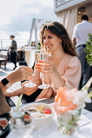 Two Women friends eating fresh oysters and drinking chilled prosecco wine on the summer sunset in...