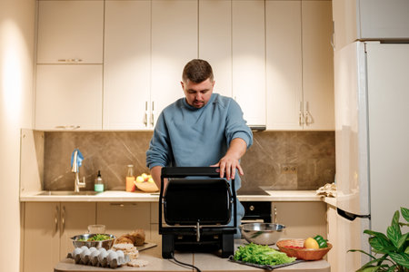 Man prepares delicious juicy meat steak on an electric grill on wooden table. Smoke in the home kitchenの写真素材