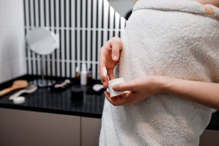 Close up of female hands taking moisturizing cream from bottle in bathroom. Woman taking care of her dry complexionの写真素材