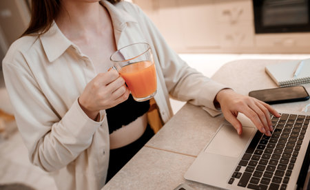Businesswoman working at home office on laptop and drink juice. Young happy female student studying in online universityの写真素材