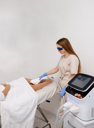 Beautician making hair removing procedure on legs for woman client. Laser epilation and cosmetology in beauty salonの写真素材