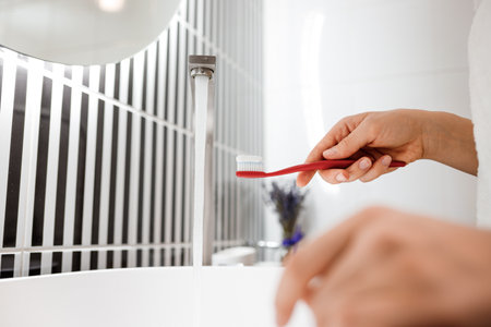 Close up of woman hand holding toothbrush with toothpaste while standing in bathroomの写真素材