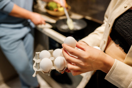 Lovely cheerful couple rejoicing while cooking breakfast with eggs together in modern kitchenの写真素材