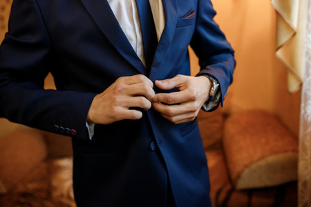 groom buttoning his blue suit before the wedding ceremony in the roomの写真素材