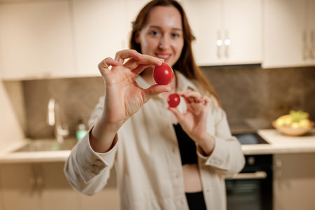 Healthy food concept. Young happy woman holding cherry tomato and smiling on background of modern white kitchen. Home cooking, salad ingredientsの写真素材