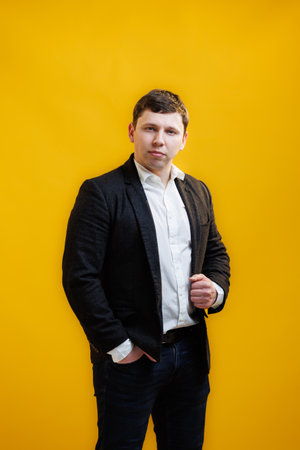 Portrait of focused businessman wearing suit standing on yellow studio background and looking at...