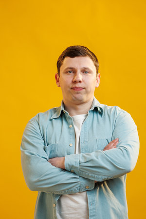 Portrait of handsome european man in shirt looking at camera standing on yellow studio background