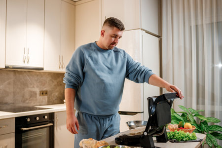Man prepares delicious juicy meat steak on an electric grill on wooden table. Smoke in the home...