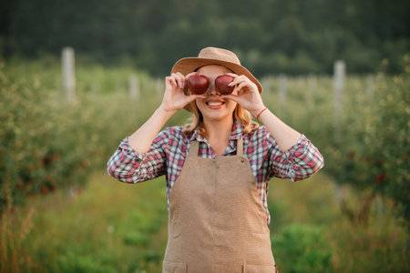 Happy smiling female farmer worker holding picking fresh ripe apples in orchard garden during autumn...