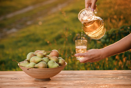 Woman's hand pouring fresh tasty pear juice in glass with natural orchard background on sunset light. Vegetarian fruit compositionの写真素材