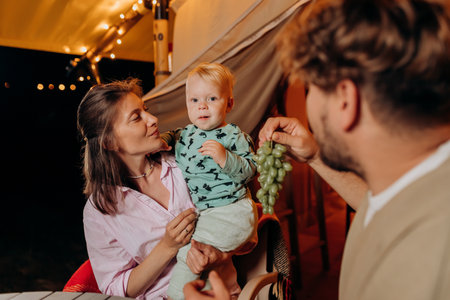 Happy family with lovely baby have dinner and spend time together in glamping on summer evening near cozy bonfire. Luxury camping tent for outdoor recreation and recreation. Lifestyle conceptの写真素材