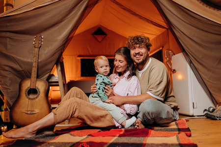 Happy family with lovely baby playing and spend time together in glamping on summer evening. Luxury camping tent for outdoor recreation and recreation. Lifestyle conceptの写真素材