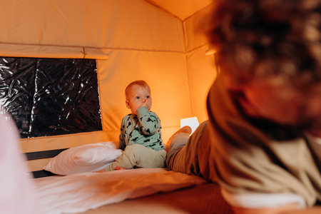 Happy family with lovely baby playing and spend time together in cozy glamping on summer evening while lying on bed. Luxury camping tent for outdoor recreation and recreationの写真素材