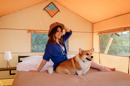 Happy woman in hat with Welsh Corgi Pembroke dog relaxing in glamping on summer day. Luxury camping tent for outdoor recreation and recreation. Lifestyle conceptの写真素材