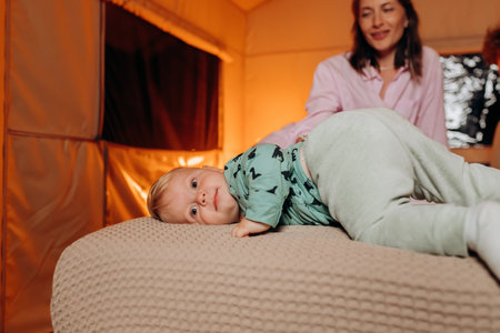 Happy family with lovely baby playing and spend time together in cozy glamping on summer evening while lying on bed. Luxury camping tent for outdoor recreation and recreationの写真素材