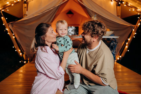 Happy family with lovely baby relaxing and spend time together in glamping on summer evening near cozy bonfire. Luxury camping tent for outdoor recreation and recreation. Lifestyle conceptの写真素材