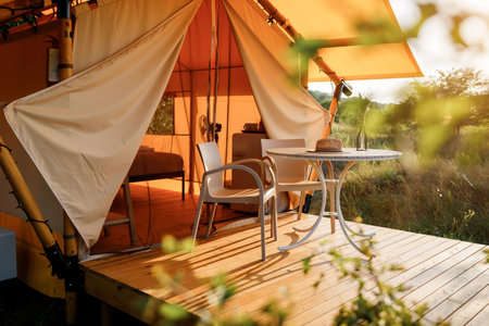 Cozy open glamping tent with light inside during sunset. Luxury camping tent for outdoor summer...