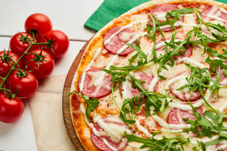 Freshly baked tasty pepperoni pizza with salami, mozzarella cheese and rukkola served on wooden background with tomatoes, sauce and herbs. Food delivery concept. Restaurant menuの写真素材