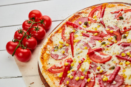 Freshly baked tasty pepperoni pizza with salami, mozzarella cheese, corn and pepper served on wooden background with tomatoes, sauce and herbs. Food delivery concept. Restaurant menuの写真素材