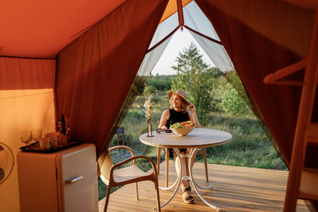Happy Woman freelancer in sunglasses relaxing on cozy glamping tent in sunny day. Luxury camping tent for outdoor summer holiday and vacation. Lifestyle conceptの写真素材