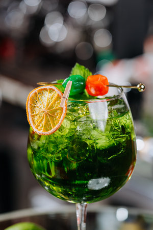 Close-up of a vibrant green cocktail with orange garnish and colorful skewer in a glass full of iceの写真素材