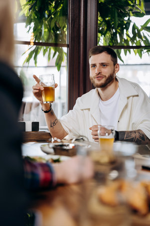 Happy young man drinking draft beer while having fun in pub or bar with friends and laughing
