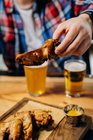 Male hand holding spicy grilled BBQ chicken wings and eating with beer in pubの写真素材