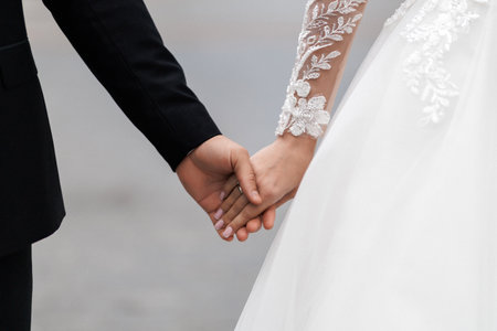 Bride and groom with bands holding hands and touching during their wedding ceremony