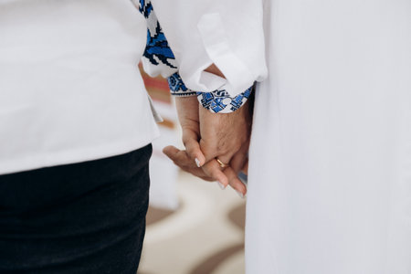 Bride and groom in Ukrainian style clothes with bands holding hands during wedding ceremony
