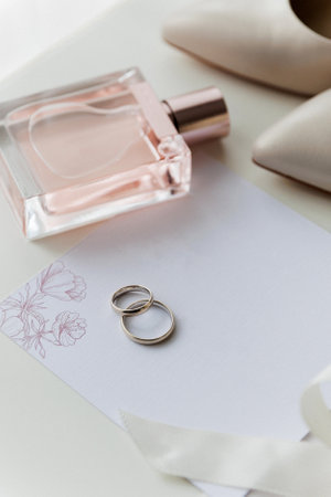 Brides wedding essentials: heels, bouquet, rings, perfume, and invitation on a white tableの写真素材