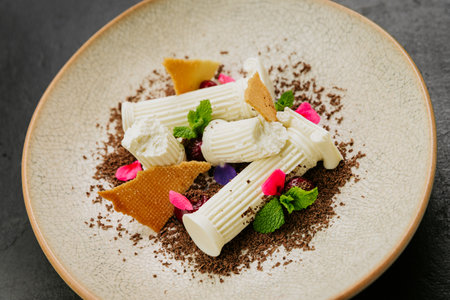 Gourmet dessert with white chocolate, biscuit shards, mint, and edible flowers on a textured plate